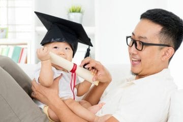 A Baby Wearing A Graduation Cap With A Man Sitting On The Couch, Emphasizing flexibility in grades during homeschool