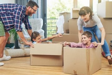 A Family Moving Into A New Home And Playing With Cardboard Boxes.