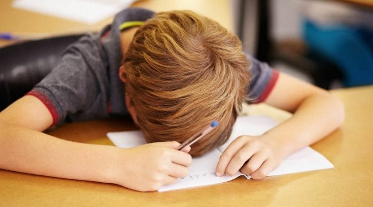 A Boy Is Sitting At A Desk And Writing On A Piece Of Paper, Experiencing School Anxiety Relief.