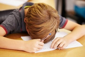 A Boy Is Sitting At A Desk And Writing On A Piece Of Paper, Experiencing School Anxiety Relief.