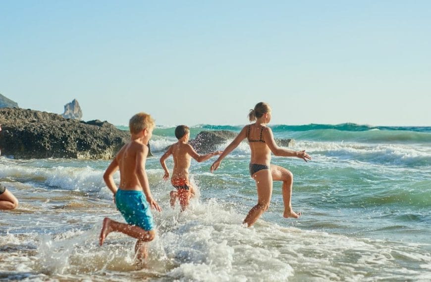 A Group Of Children Running And Having Fun In The Ocean During Homeschool Summer Break.