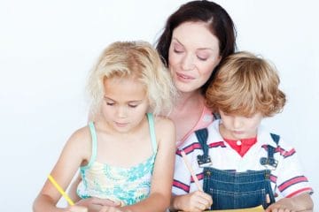 A Mother And Two Children Are Working On A Piece Of Paper.