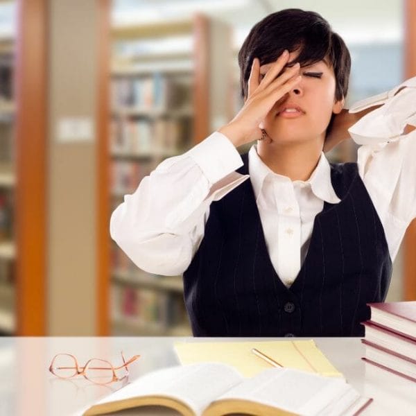 A Woman Covering Her Eyes In Front Of Books In A Library.