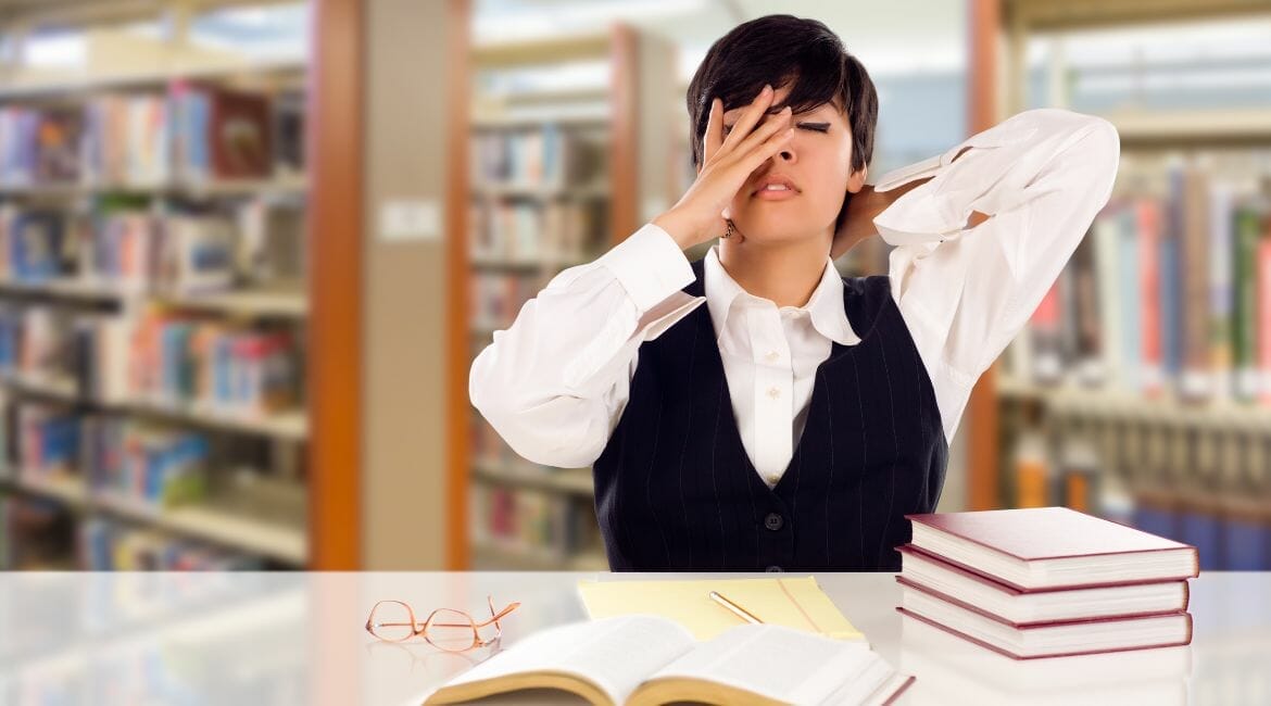 A Woman Covering Her Eyes In Front Of Books In A Library.