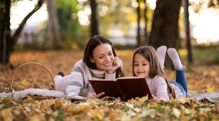 A Mother And Daughter Reading A Book In A Park.