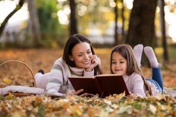 A Mother And Daughter Reading A Book In A Park.