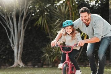 A Man And A Girl Riding A Bike In A Park.